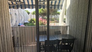 A covered outdoor area with a table and chairs, a sliding glass door, and a view of a garden with pink flowers and a water feature.