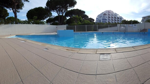 A swimming pool with a tiled deck, surrounded by a low wall and a fence.