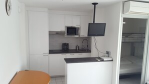 A compact kitchen with white cabinets, a microwave, a coffee maker, and a flat-screen TV mounted above the counter.