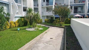 A courtyard with a pathway, surrounded by greenery and a building with balconies.