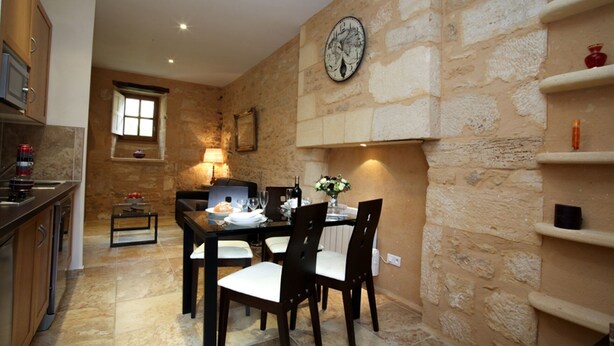 A dining area with a stone wall, a clock, and a table set for four. - APARTMENT THE THREE FOUNTAINS (Sarlat-La-Canéda)