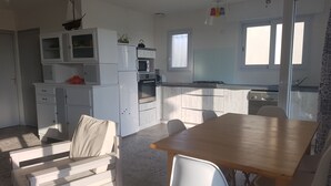 Une cuisine compacte avec des meubles blancs, un four à micro-ondes et une cuisinière. On y trouve également un coin repas avec une table en bois et des chaises blanches.