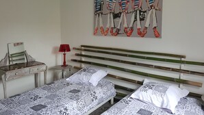 Une chambre avec deux lits, une lampe rouge, un tableau accroché au mur et un miroir posé sur la commode.