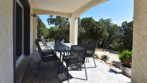 An outdoor patio with a glass table and chairs, surrounded by a stone floor and a view of trees. - SUPERB RENT ANY COMFORT - POOL - BOULODROME - PRIVATE PARKING IN PEACE (Calenzana)