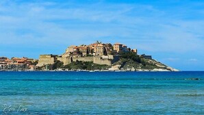 A coastal town with a prominent castle-like structure on a hill, overlooking the sea. - SUPERB RENT ANY COMFORT - POOL - BOULODROME - PRIVATE PARKING IN PEACE (Calenzana)