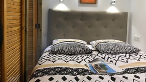 Una cama bien tendida con ropa de cama estampada, cabecero con diseño acolchado y dos lámparas fijadas a la pared.