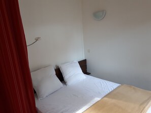 Un lit simple avec une literie blanche et une tête de lit marron, dans une pièce aux murs blancs.