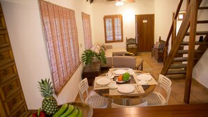 A dining area with a wooden table set for two, surrounded by white chairs. A wooden staircase is visible to the right, leading to an upper level. - A third world oasis on the idyllic beach of Santa Clara. (Santa Clara)