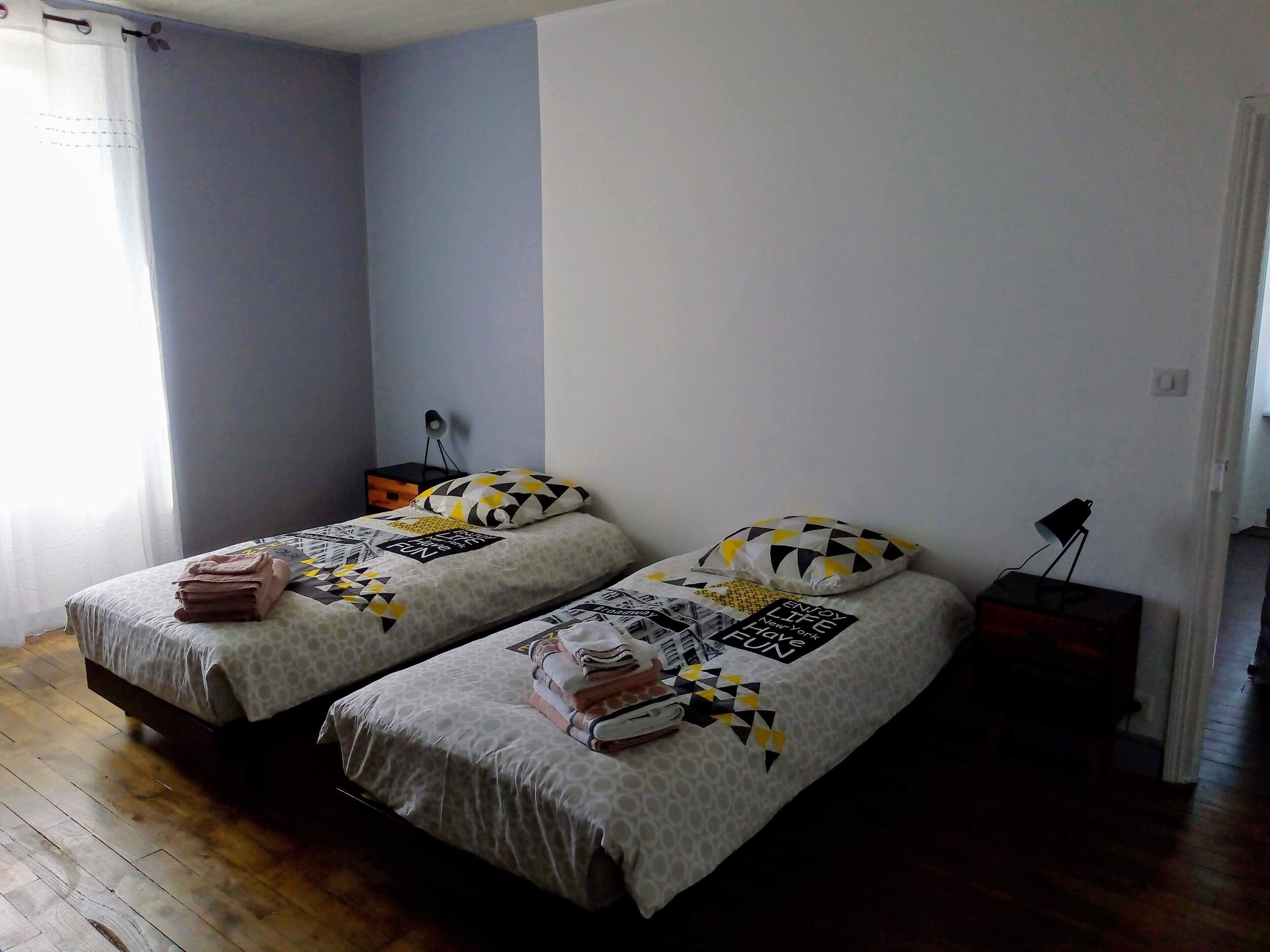 Une chambre avec deux lits, chacun agrémenté de draps et d’oreillers à motifs, une table de chevet avec une lampe et une fenêtre avec des rideaux.