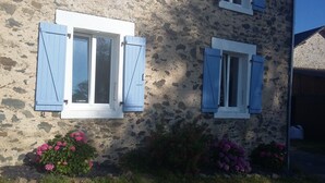 Ein Steinhaus mit zwei Fenstern und blauen Fensterläden.