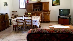 Un comedor con una mesa preparada para cuatro personas, rodeada de sillas de madera. Un televisor está montado en un mueble a la derecha.