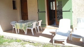 Un patio con una mesa, sillas, una puerta y una ventana con contraventanas.