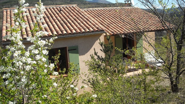 Una casa con techo de tejas, rodeada de follaje y plantas florecientes.