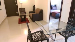 Relax in a comfortable space with a glass-top dining table, dark brown sofa, and plush bed.