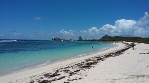 A beach with clear turquoise water, white sand, and rocky outcrops in the distance. - charming little 2 bedroom villa with private pool in residential area (SAINT FRANCOIS)