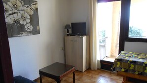 Una habitación pequeña con sofá, una mesa, un mueble con televisor y una ventana con cortinas.