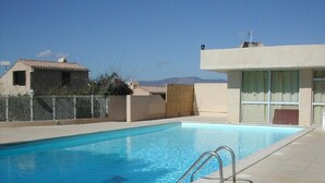 Piscina rectangular con escalera metálica, rodeada por un solárium con baldosas.