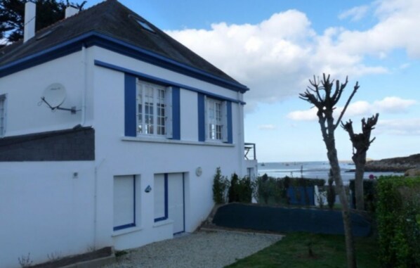A white building with blue trim and a door, located near a body of water. - Quiet, 30 meters from a beautiful beach in Kersaint (Landunvez)