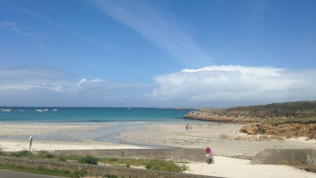 A beach with a clear sky, calm sea, and rocky outcrops.