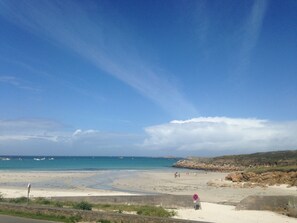 Une plage avec un ciel dégagé, une mer calme et des affleurements rocheux.