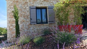 Un edificio in pietra con tetto in tegole, una finestra con persiane e un giardino con piante di lavanda.