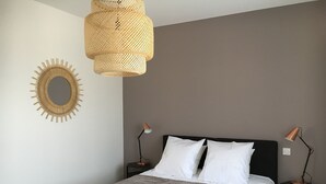 Una camera da letto con un letto, due comodini, una lampada, uno specchio a parete e una lampada a sospensione.