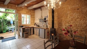 A rustic kitchen with a stone wall, wooden beams, a built-in stove, and a chandelier.