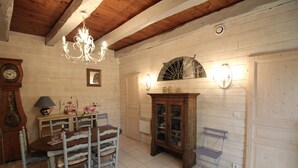 A rustic room with a wooden ceiling, a chandelier, a dining table with chairs, a cabinet, and a clock.