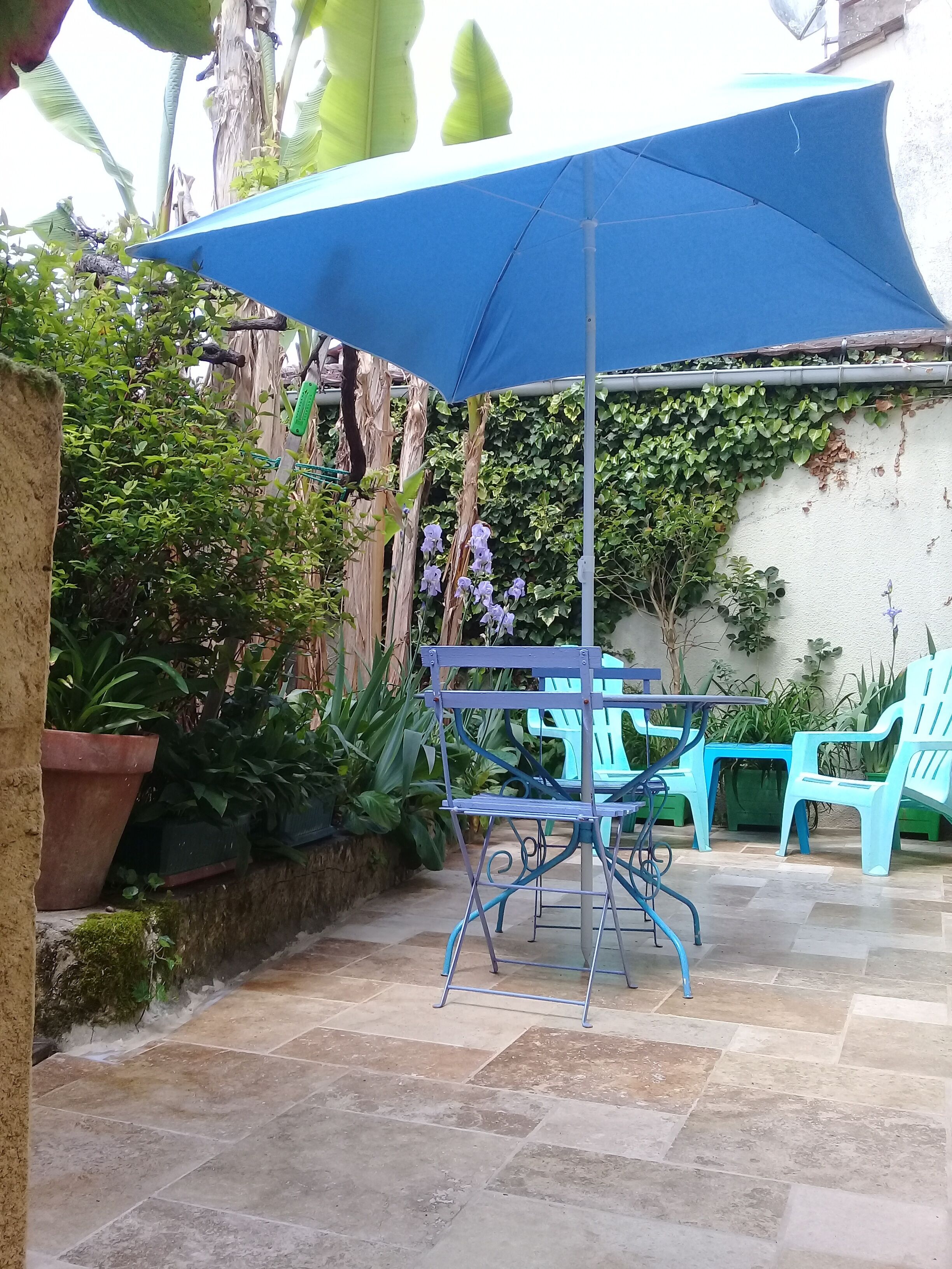Un'area patio con un ombrellone blu, un tavolo in metallo e sedie di plastica blu.