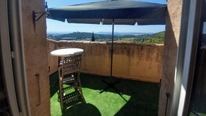 A balcony with a table and chairs, an umbrella, and a view of the countryside. - Apartment Sea View Balcony & Shared Pool Air Conditioning (Hyères)