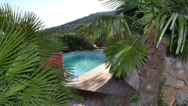 A wooden deck leading to a swimming pool surrounded by lush greenery and a stone wall. - Apartment Sea View Balcony & Shared Pool Air Conditioning (Hyères)