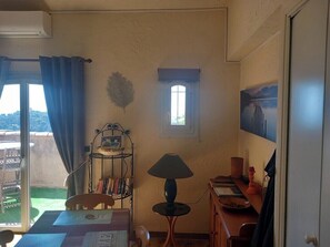 A room with a table, a chair, a lamp, a window, and a door. - Apartment Sea View Balcony & Shared Pool Air Conditioning (Hyères)