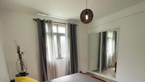 Une chambre à coucher avec un lit, des rideaux, un miroir et un luminaire suspendu.