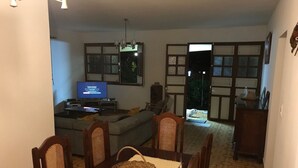 Un coin repas avec une table dressée pour quatre personnes, un téléviseur en arrière-plan et une vue sur un salon avec un canapé et une table à manger.
