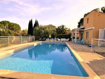 La grande piscine, et sa terrasse avec chaises longues et mobilier de jardin