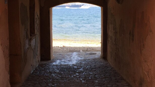 Ein schmaler, mit Kopfsteinpflaster belegter Weg führt durch einen Bogen hindurch zum Strand.
