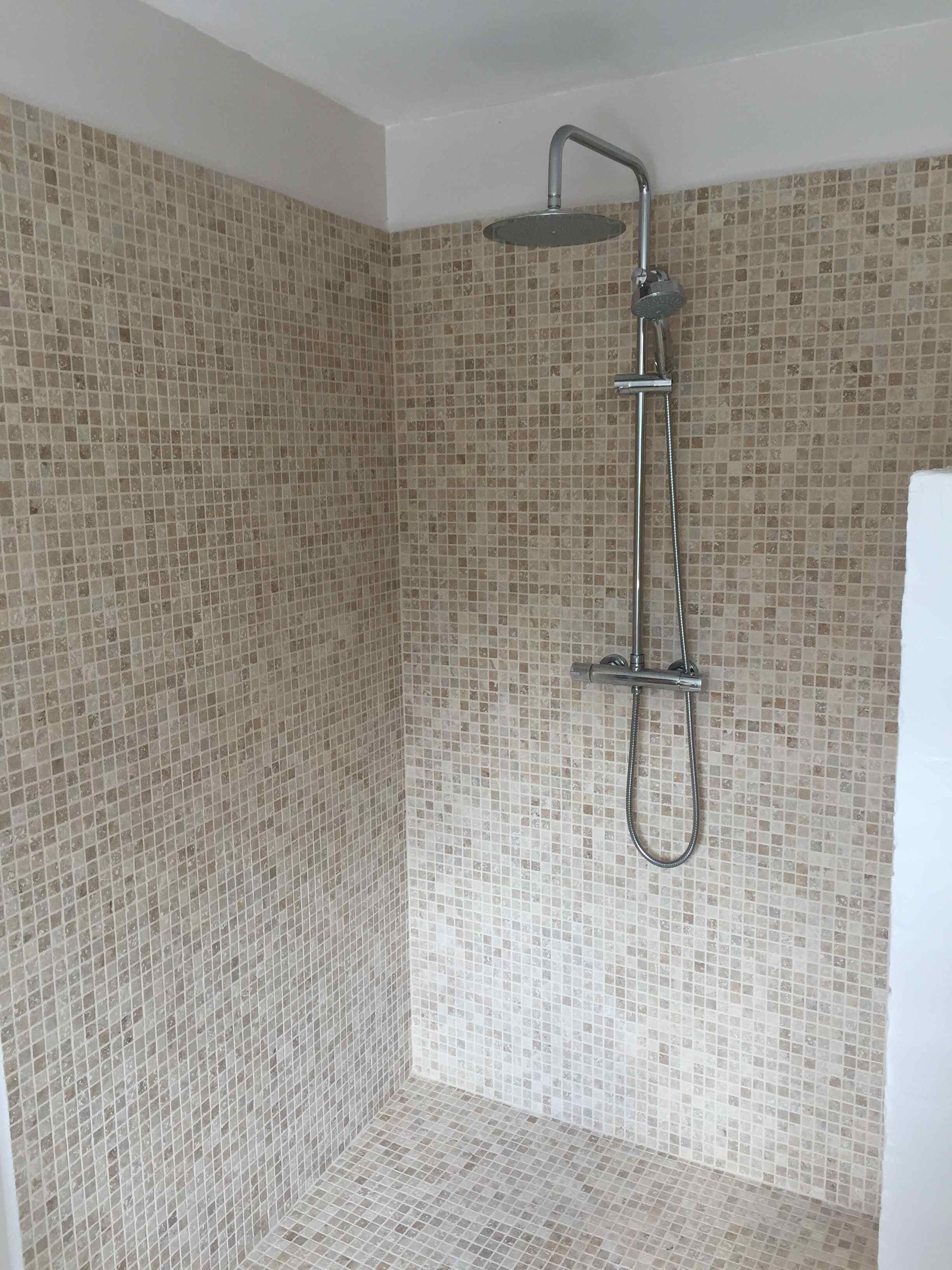 A shower with a handheld showerhead and a fixed showerhead, tiled walls, and a white ceiling.