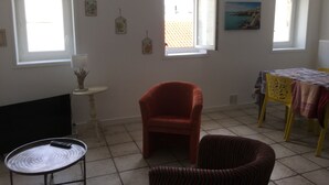A room with two windows, a table with a tablecloth, a chair, and a lamp on a small table.