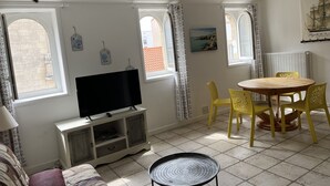 A room with a TV on a cabinet, a dining table with yellow chairs, and a window with a view of buildings.