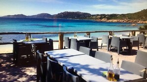 Un espace de restauration en plein air, avec des tables et des chaises, offrant une vue sur une plage et la mer.