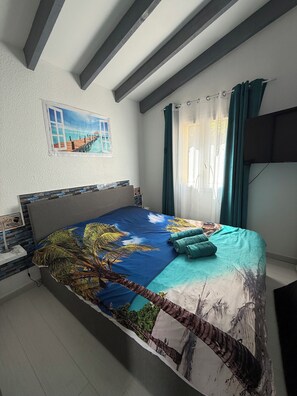 A bedroom with a bed, a nightstand, a TV, a painting, and a window with curtains. - Mini villa F2 tt furnished 42m2 sea view santa giulia (Porto-Vecchio)