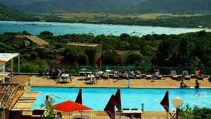 Un espace piscine doté de chaises longues et de parasols, offrant une vue sur un plan d’eau et des collines.