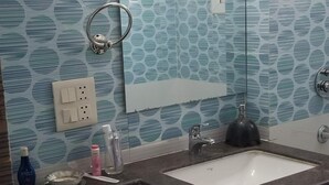 A bathroom with a white toilet, a sink with a mirror above it, and a shower area. - The most homely place in Noida (Sector 137)