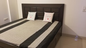 A neatly made bed with a striped bedspread and two decorative pillows. - The most homely place in Noida (Sector 137)
