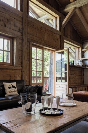 A wooden interior with a dining table set for a meal, a bottle of wine, and several glasses.