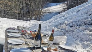 A wooden picnic table set outdoors with plates, glasses, and bottles of wine, surrounded by snow and trees. - Exceptional "Frachette" Chalet (Praz-Sur-Arly)
