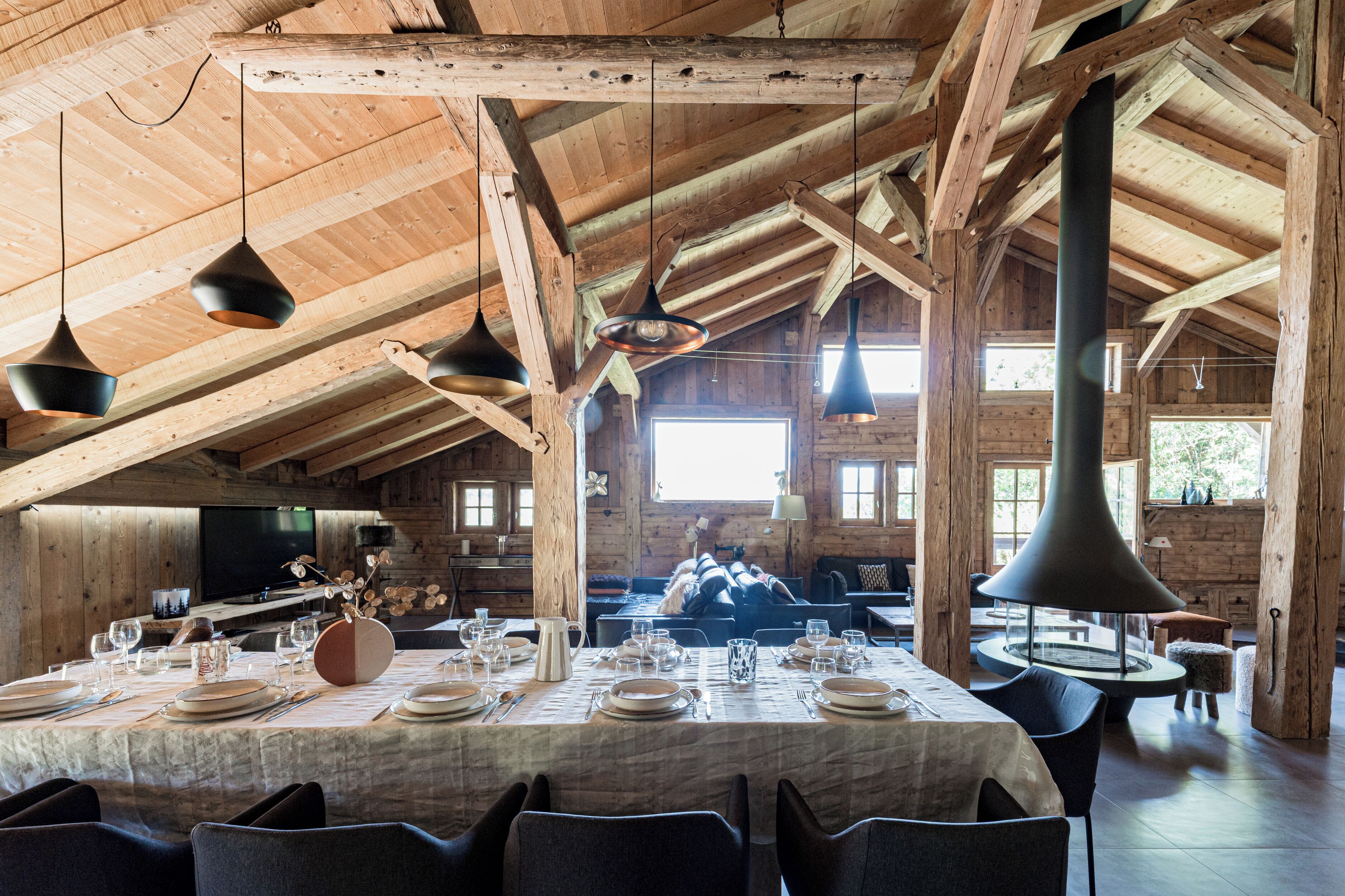 Une salle à manger spacieuse, dotée d’un plafond haut et de poutres apparentes, où une longue table est dressée pour le repas.