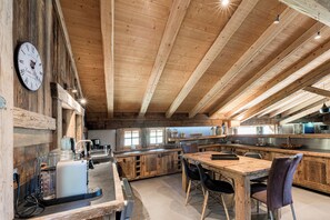 A rustic kitchen with wooden beams, a vintage clock, and a bar area with stools.