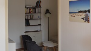 A modern living room with a dining table, chairs, a bookshelf, a lamp, and a beach-themed painting on the wall.