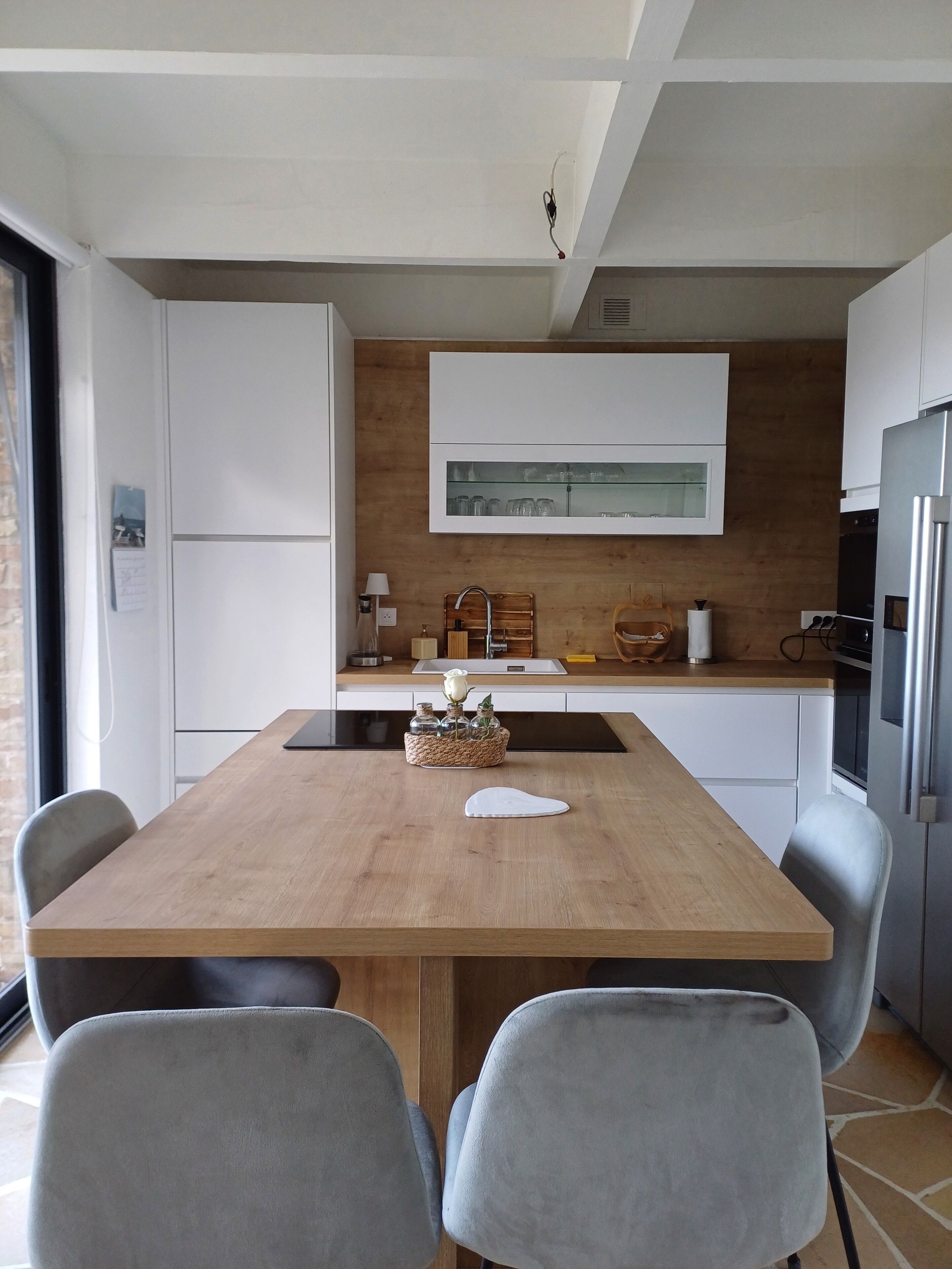 Een moderne keuken met een houten tafel, grijze stoelen en witte kastjes.